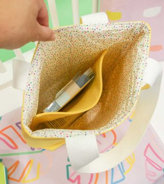 A hand holding open a polka dot lined tote bag with white canvas straps and a boxed bottom, showing the roomy inside pocket