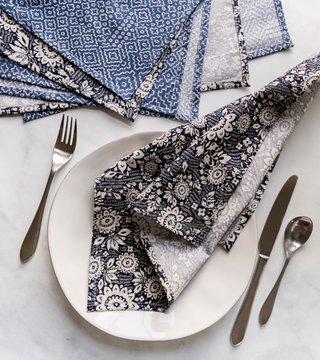 Folded navy and blue patterned cloth napkins on a white plate with cutlery, and a stack of folded napkins beside it