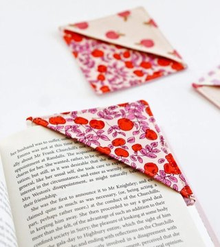 A floral fabric corner bookmark tucked over the corner of an open book page, with two more folded bookmarks in the background