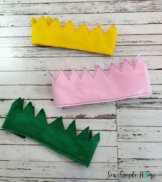 Three zigzag-edged felt crowns in yellow, pink and green, laid flat on a whitewashed wooden background
