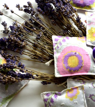 Small floral fabric lavender bags with purple ribbon ties scattered around bunches of dried lavender