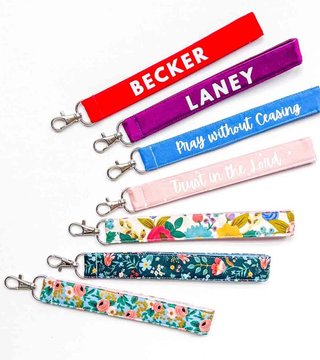 Seven fabric key fob wristlets with lobster clasps, some personalised with names and phrases, in solid colours and florals