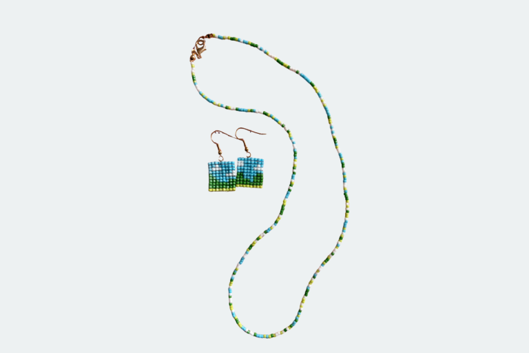 A handmade square-stitch beaded pendant made from cylinder beads, held between finger and thumb outdoors