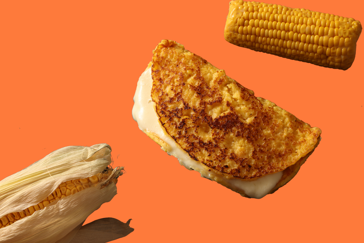 A cachapa folded over melting cheese, with a corn cob and husk beside it